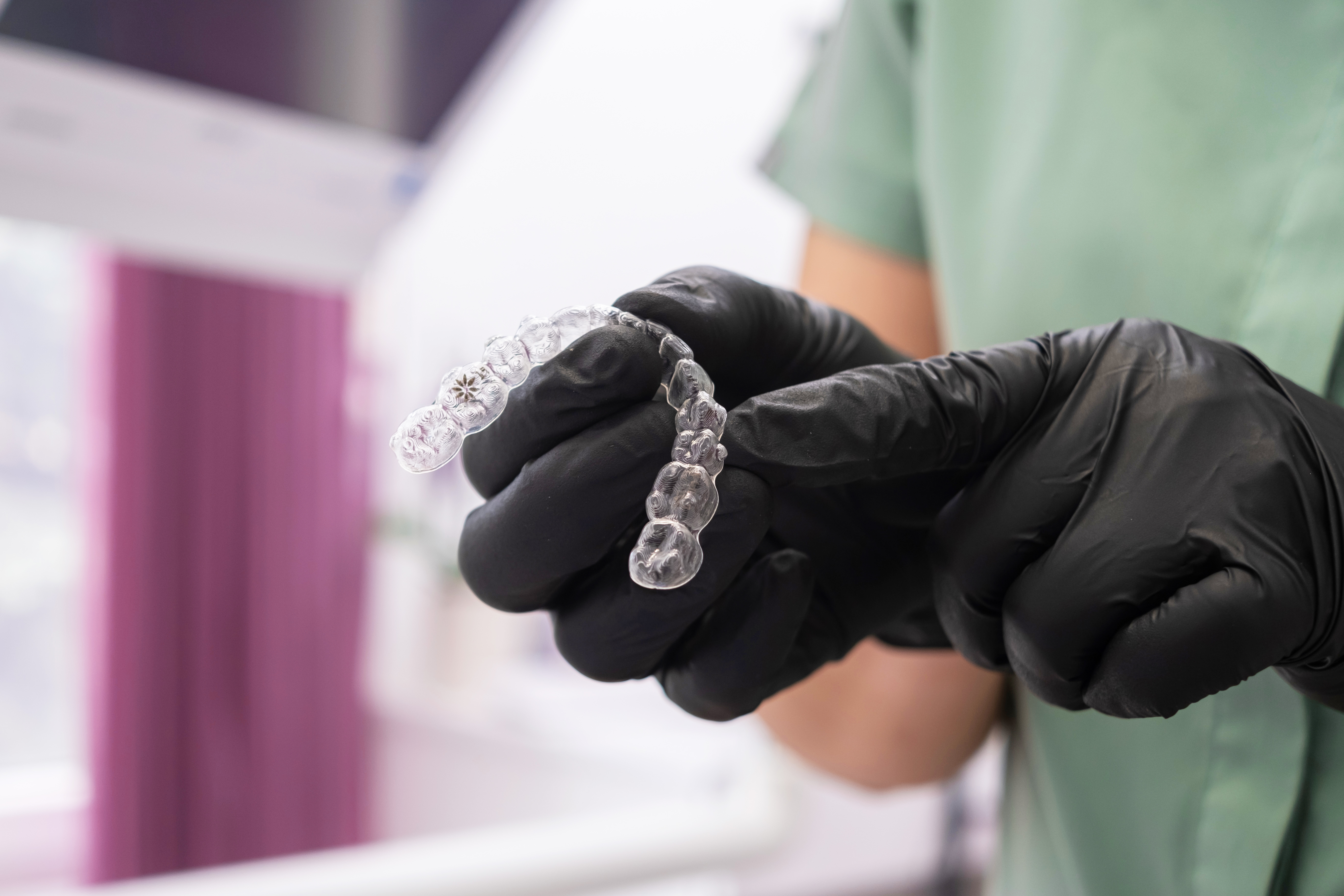 A close-up of hand grasping an invisible dental aligner retainer at a dental clinic